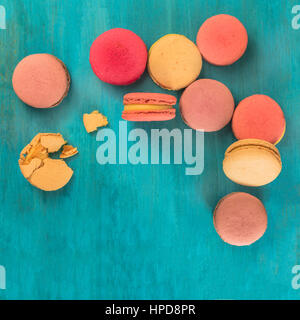 A square photo of various macarons, shot from above on a vibrant blue background texture, with crumbs and copyspace Stock Photo