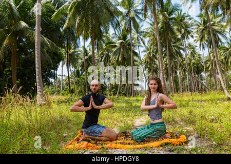Young couple doing yoga surrounded by palm trees Stock Photo