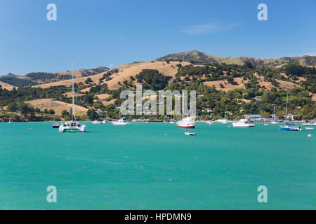 Akaroa, Canterbury, New Zealand. View across the turquoise waters of Akaroa Harbour to the rolling hills of the Banks Peninsula. Stock Photo