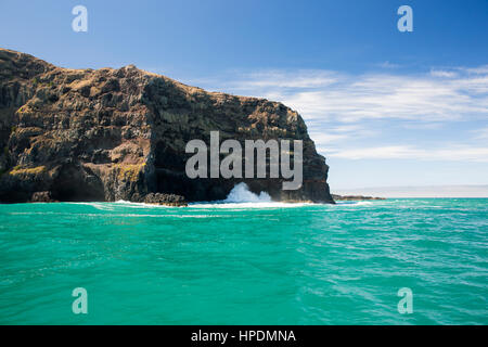 Akaroa, Canterbury, New Zealand. View across the turquoise waters of the Pacific Ocean to to the rugged cliffs of Akaroa Head. Stock Photo