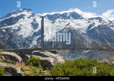 Aoraki/Mount Cook National Park, Canterbury, New Zealand. Hiker crossing suspension bridge on the Hooker Valley Track, Mount Sefton in background.