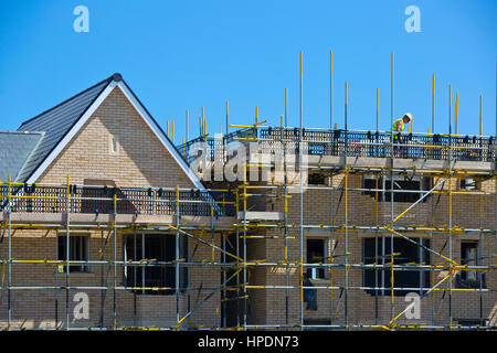 New housing development with construction worker in hard hat on scaffolding against a bright blue sky working on the roof timbers Stock Photo