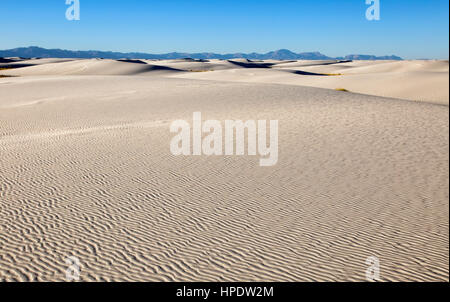 White sand dunes stretch out to the horizon on a blue sky day. Taken at White Sands National Monument in New Mexico. Stock Photo