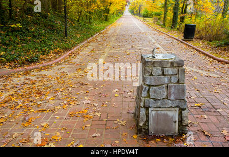 A stone water fountain on brick walking path during the colorful fall season. Take at Hot Spring National Park in Arkansas. Stock Photo
