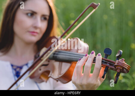 Young woman playing violin in a field at sunset Stock Photo