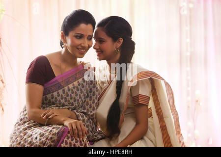 Smiling teenage girl in sari whispering to mother Stock Photo