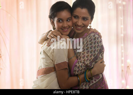 Smiling teenage daughter in sari and mother hugging Stock Photo