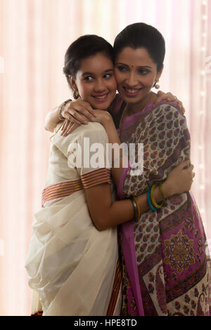 Smiling teenage daughter in sari hugging mother Stock Photo