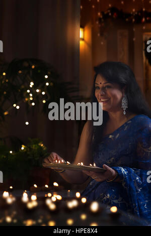 Happy indian woman in traditional sari arranging oil lamp during diwali festival Stock Photo