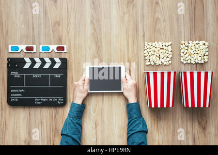 Man watching movies streaming online using a digital tablet, popcorn, 3D glasses and clapboard, cinema and entertainment concept Stock Photo