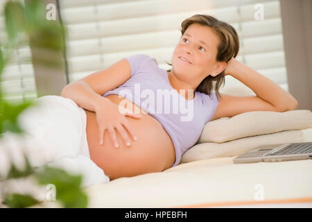 Model released , Hochschwangere Frau liegt gemuetlich am Bett, Laptop steht daneben - pregnant woman with laptop relaxing in bed Stock Photo