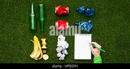 Waste sorting and separate garbage collection concept, tidy rubbish on the grass divided by material and man writing on a notepad, top view Stock Photo