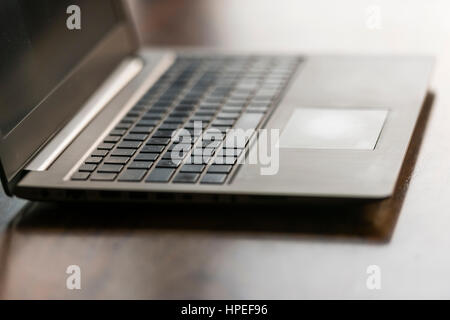 Opened laptop computer on a wooden desk. Focus on touchpad, backlight, no people Stock Photo
