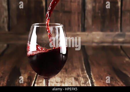 Red wine is poured from bottle to glass on wooden background Stock Photo
