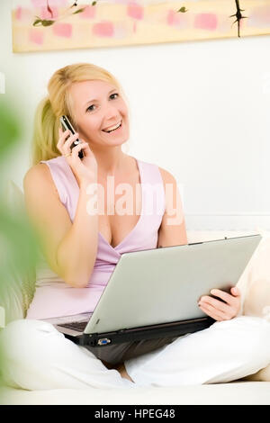 Model released , Junge Frau, 35, mit Laptop auf der Couch telefoniert mit Handy - woman using laptop at home