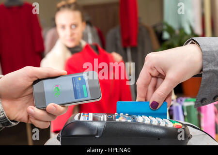 Near Field Communication - Man completing mobile Payment Woman shopping, male Hand holding cell Phone making instant Transaction at checkout Terminal  Stock Photo