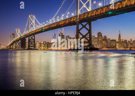 Classic panoramic view of famous Oakland Bay Bridge with the skyline of San Francisco illuminated in beautiful twilight after sunset in summer, USA Stock Photo