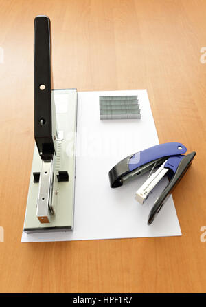 Big and small staplers with staples and paper on wood table Stock Photo