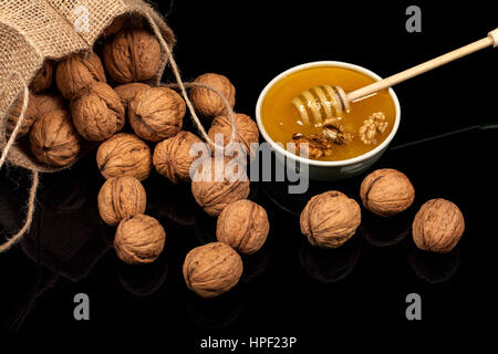 Walnuts in the bag of burlap. Spilling nuts lie on a glossy surface on a black background Stock Photo
