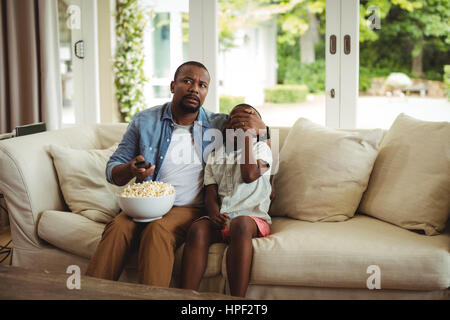 Father covering sons eyes while watching television at home Stock Photo