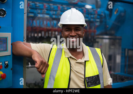 Portrait of smiling factory worker leaning on machine control cabinet in factory Stock Photo