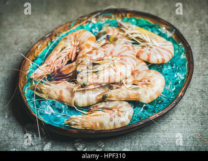 Raw uncooked tiger prawns on chipped ice in turquoise blue tray over grey concrete background, selective focus, horizontal composition. Fresh seafood Stock Photo