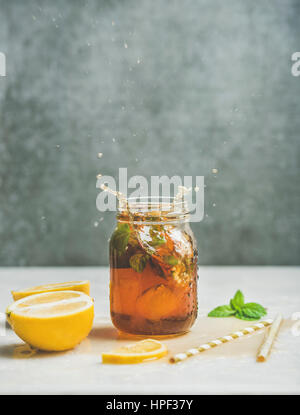 Summer cold Iced tea with fresh bergamot, mint and lemon in glass jar with splashes on light table, grey concrete wall at background, copy space. Food Stock Photo