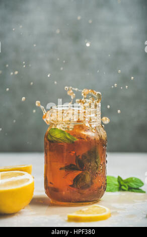 Summer cold Iced tea with fresh bergamot, mint and lemon in glass jar with splashes, grey concrete wall at background, copy space. Food in motion conc Stock Photo