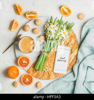 Cup of morning coffee, cookies, red oranges and bucket of spring flowers and mobile phone with text Good morning on board over light grey marble backg Stock Photo