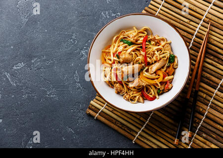 Udon stir-fry noodles with chicken in bowl on dark stone background copy space Stock Photo