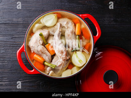 Stewed rabbit with potatoes and carrot in cast iron pan on black burned wooden background Stock Photo