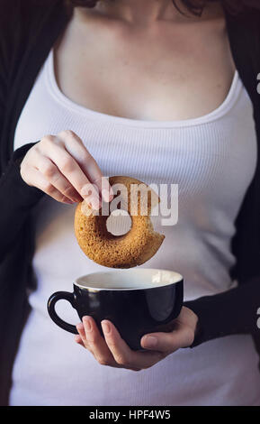 Breakfast time: woman holding in her hands a donut and a cup of coffee Stock Photo