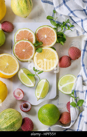 Variety of whole and sliced citrus fruits pink tiger lemon, lemon, lime, mint and exotic lichee on white chopping board with kitchen towel over white Stock Photo