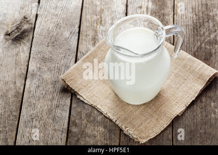 glass jug with milk on wooden background. Jug of milk on wooden table. Milk jug with napkin on old wooden table, copy space Stock Photo