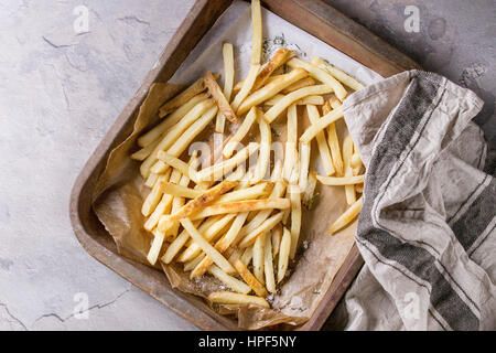 Fast food french fries potatoes with skin served with salt on baking paper in old rusty oven tray with kitchen towel over gray texture background. Top Stock Photo