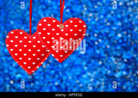 two sewn hearts hanging against blue bokeh background. Valentine theme - red felt hearts with thread. Decorative textile hearts Stock Photo