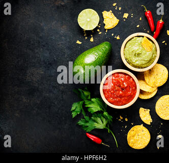 Mexican food concept: tortilla chips, guacamole, salsa and fresh ingredients over vintage rusty metal background. Top view Stock Photo
