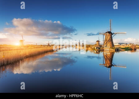 Windmills at sunrise. Rustic landscape with amazing dutch windmills near the water canals with blue sky and clouds reflected in water Stock Photo