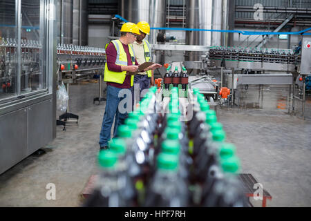 Two factory workers monitoring cold drink bottles on production line at drinks production plant Stock Photo