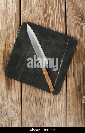 Knife on black slate plate against wooden background Stock Photo