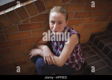 Portrait of sad schoolgirl sitting alone on staircase in school Stock Photo