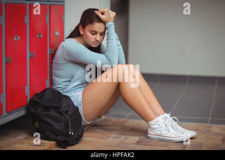 Sad schoolgirl sitting in locker room at school Stock Photo