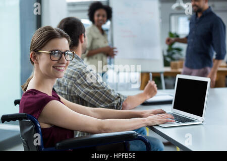 Portrait of smiling business executive in wheelchair working on laptop in meeting at office Stock Photo