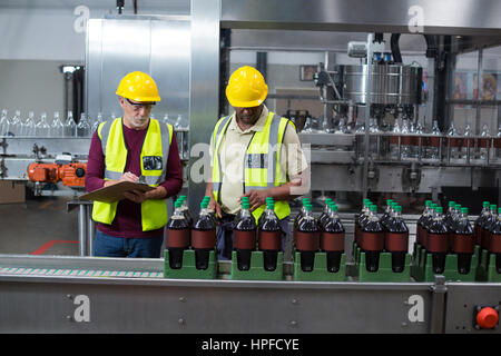 Two factory workers monitoring cold drink bottles at drinks production plant Stock Photo