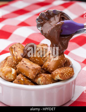 A close up image of a bowl of small pretzels with chocolate frosting on a spoon. Stock Photo