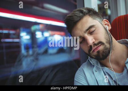 Executive sleeping while listening music in train Stock Photo