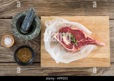 Raw Rib chop, rosemary herb, salt, corainder seeds and stone grinder against wooden background Stock Photo