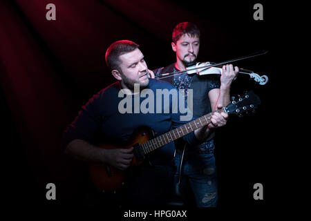 Two bearded men playing on electric guitar and electro violin on a black background Stock Photo