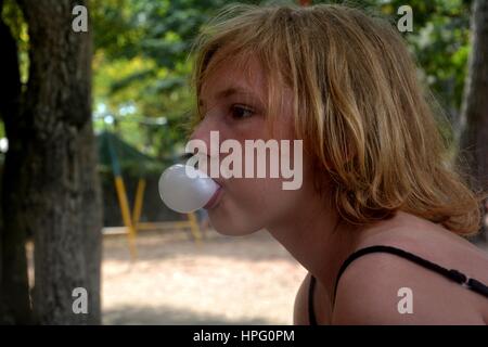 Girl of the side makes a small bubble with chewing gum Stock Photo