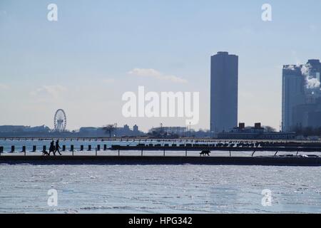 Pedestrians and dogs walk on pier jutting into a frozen Lake Michigan with the great Chicago skyline and Navy Pier attraction holding up the backgroun Stock Photo